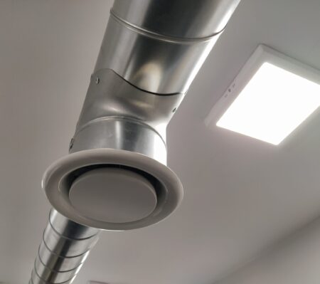 Extractor hood in a public toilet. Round metal pipe with gray air extractor. Engineering ventilation systems. Galvanized pipes under the ceiling of the room. Plastic round tip.